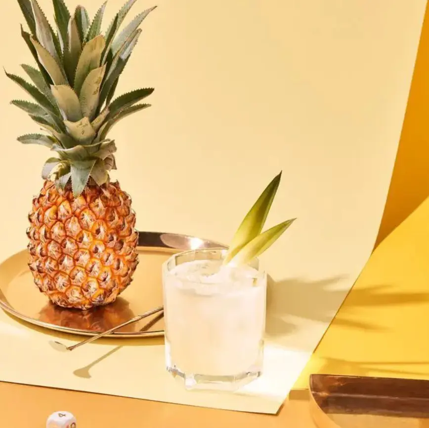 A pineapple and a glass of water on a table.