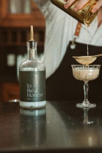 A bottle and glass on a table with a person in the background.