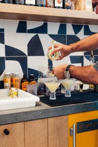 A person pouring drinks into glasses on top of a counter.