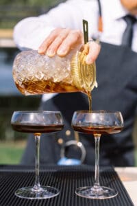 A person pouring liquid into two wine glasses.