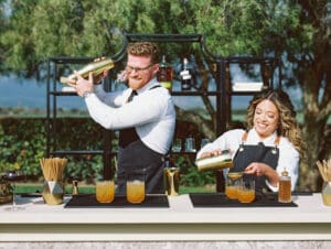 A man and woman are pouring drinks at an outdoor bar.