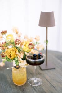 A vase of flowers and a drink on a table.